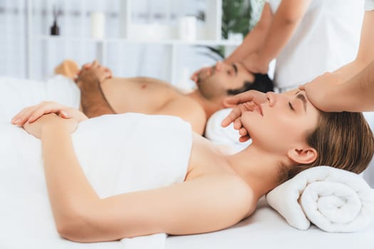 Caucasian couple enjoying relaxing anti-stress head massage and pampering facial beauty skin recreation leisure in dayspa modern light ambient at luxury resort or hotel spa salon. Quiescent