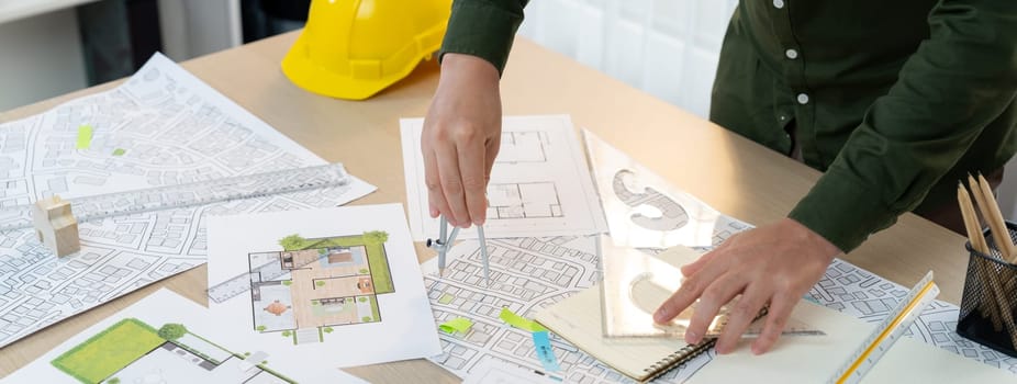 A portrait of architect using divider to measure blueprint. Architect designing house construction on a table at studio, with architectural equipment scattered around. Focus on hand. Delineation