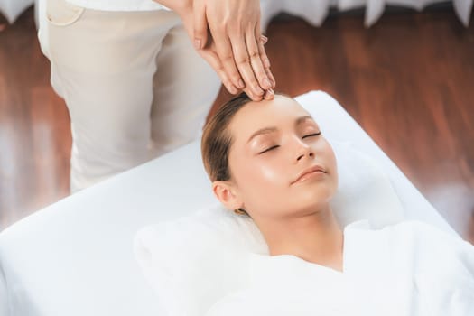 Caucasian woman enjoying relaxing anti-stress head massage and pampering facial beauty skin recreation leisure in dayspa modern light ambient at luxury resort or hotel spa salon. Quiescent