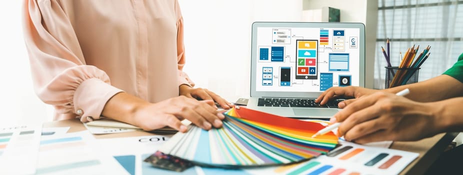 Cropped image of interior designer chooses color from color swatches while laptop displayed UI and UX designs for mobiles app and website. Creative design and business concept. Variegated.