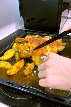 Hands cut baked chicken with potatoes with a knife. High quality photo