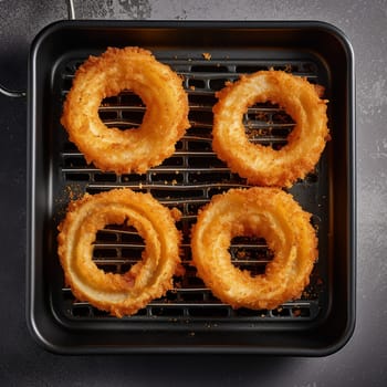 Four golden-brown onion rings on a black grill pan.