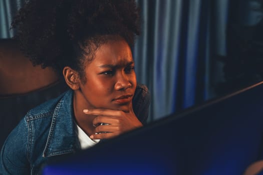 Young African American creator woman with serious face, thinking carefully and looking at final project document on laptop for planing next sequence. Concept of work at neat home place. Tastemaker.