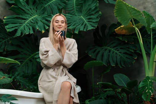 Tropical and exotic spa garden with bathtub in modern hotel or resort with woman in bathrobe holding beauty skincare product while enjoying leisure lush with greenery foliage background. Blithe