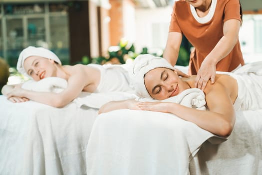 A portrait of two young attractive woman lie on bed during having back massage by a professional masseur at outdoor surrounded by peaceful natural environment. Healthy and beauty concept. Tranquility.