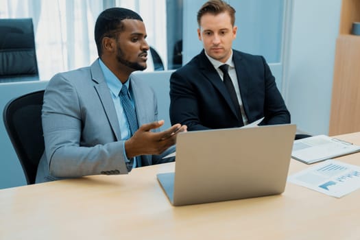 African male leader explain strategy while show solution to professional project manager by pointing at document, using laptop. Skilled business team brainstorming idea. Business meeting. Ornamented.