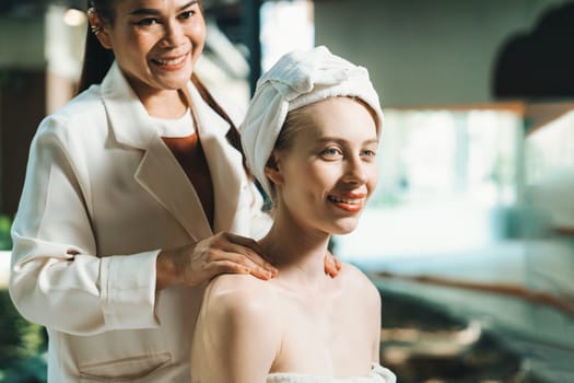 Attractive caucasian women receives back massage with smile face by Thai professional masseur while sitting surrounded by peaceful spa environment. Healthy and beauty. Blurring background.Tranquility.