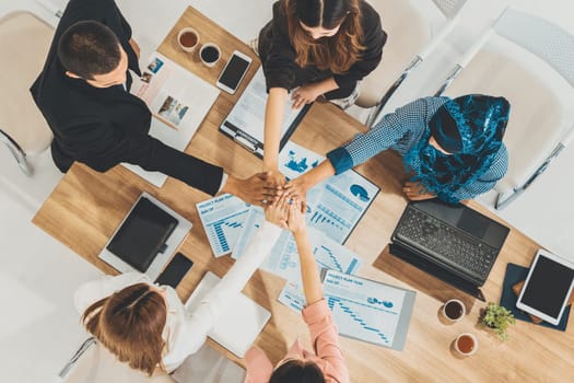 Businessmen and businesswomen joining hands in group meeting at multicultural office room showing teamwork, support and unity in business. Diversity workplace and corporate people working concept. uds