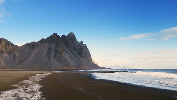 Drone shot of stokksnes beach on shore, vestrahorn mountains on icelandic peninsula with black sand beach. Beautiful nordic landscape scenery on roadside, panoramic view. Slow motion.