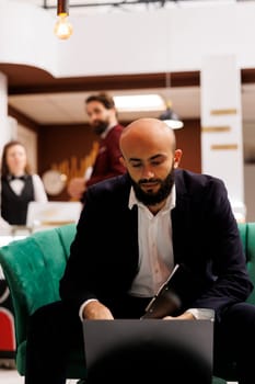 Corporate professional in lounge area waiting to meet with business CEO to discuss new colllaboration for growth. White collar worker travelling for work, using laptop in hotel lobby.