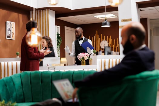 Bellhop filling in registration files for businessman arriving at hotel resort, receiving luxury concierge services. African american employee ensuring relaxing stay for guest.