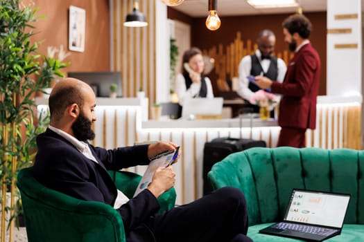 White collar worker looks at files in hotel lounge area, preparing to share new development ideas with executive board at international meeting. Young adult travelling on business trip.