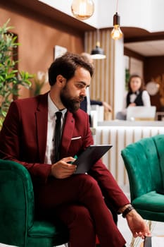 White collar worker checking files on tablet, working while he waits to do check in process at hotel. Businessman review notes before attending important meeting, business trip.