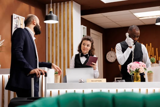 Check in process at reception counter. Front desk staff verifying passport and documents for identification in lobby, white collar worker waiting to enter room on business trip.