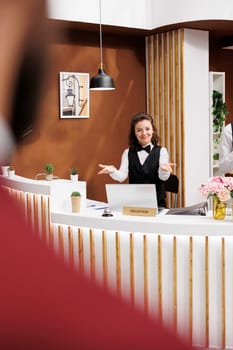 Friendly employee greeting guest in lobby, welcoming businessman at hotel reception for check in process. Front desk staff providing impeccable customer service, corporate business trip.