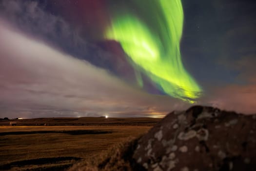 Icelandic highlands with northern lights are visible. Amazing scenery created by aurora borealis under sky full of stars. Stunning natural event with vibrant colors and snow covered rocks.