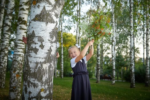 Little girl of elementary school student in modern school uniform outdoors with bouquet of flowers. Female child schoolgirl going to school. Back to school in september 1 in Russia