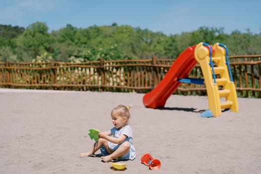 Little girl plays with plastic molds while sitting on the sand at the playground. High quality photo