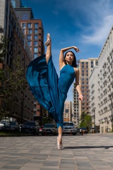 Beautiful Asian ballerina in blue dress posing in splits outdoors. Urban landscape. Vertical photo