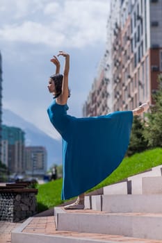 Beautiful Asian ballerina in blue dress posing on stairs outdoors. Urban landscape. Vertical photo