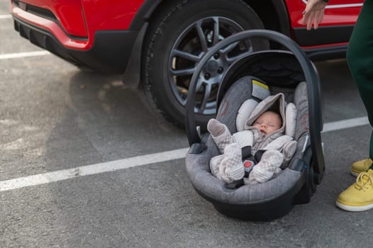 A Caucasian woman puts a child seat with a newborn baby in the car. Quick fastener