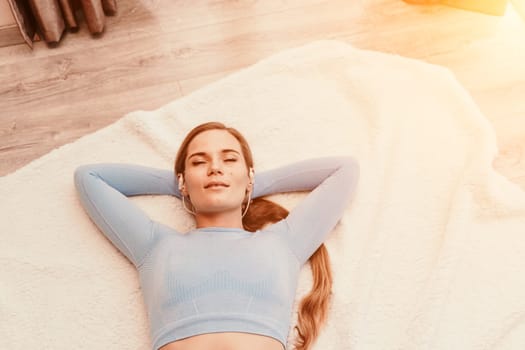 Top view portrait of relaxed woman listening to music with headphones lying on carpet at home. She is dressed in a blue tracksuit