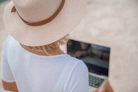 Freelance women sea working on the computer. Good looking middle aged woman typing on a laptop keyboard outdoors with a beautiful sea view. The concept of remote work