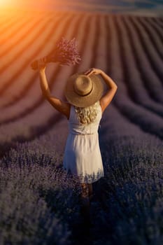 Blonde woman poses in lavender field at sunset. Happy woman in white dress holds lavender bouquet. Aromatherapy concept, lavender oil, photo session in lavender.