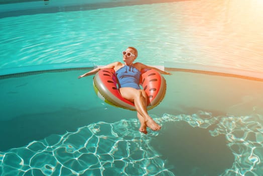 Happy woman in a swimsuit and sunglasses floating on an inflatable ring in the form of a watermelon, in the pool during summer holidays and vacations. Summer concept