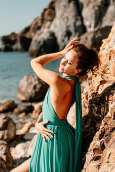 Woman green dress sea. Woman in a long mint dress posing on a beach with rocks on sunny day. Girl on the nature on blue sky background