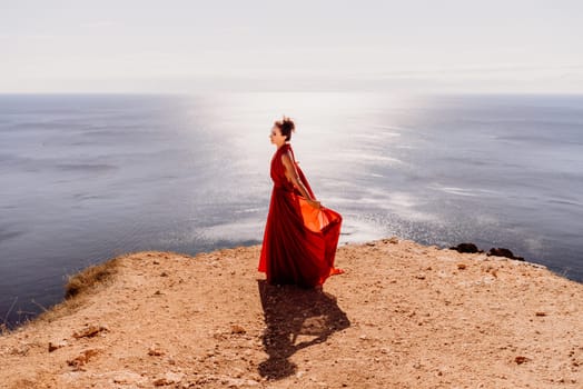 Woman red dress sea. posing on a rocky outcrop high above the sea. Girl on the nature on blue sky background. Fashion photo