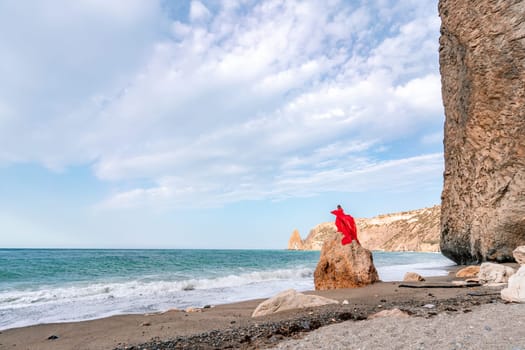 woman sea red dress. Woman with long hair on a sunny seashore in a red flowing dress, back view, silk fabric waving in the wind. Against the backdrop of the blue sky and mountains on the seashore