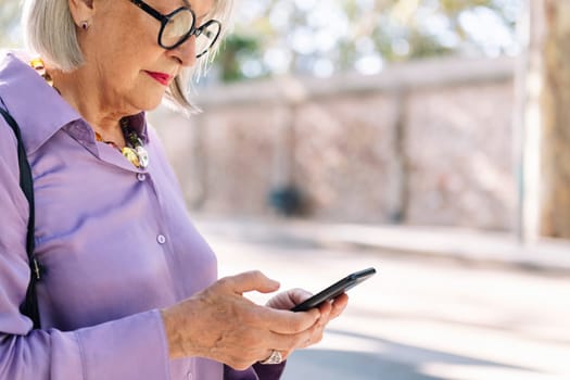 close up of a senior woman typing on mobile phone outdoors, concept of technology and elderly people leisure, copy space for text