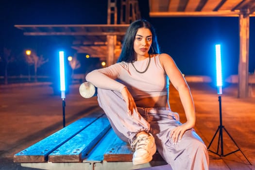 Young dancer sitting posing at night sitting in an outdoor park next to neon lights