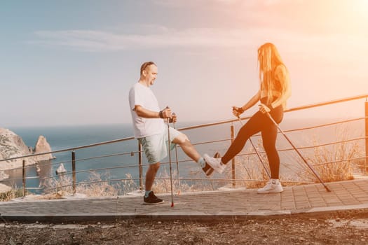 Happy Middle aged couple or friends practicing nordic walking in park near sea. Mature couple with trekking poles walking, practicing Nordic walking outdoors. Aging youthfully and sport concept.