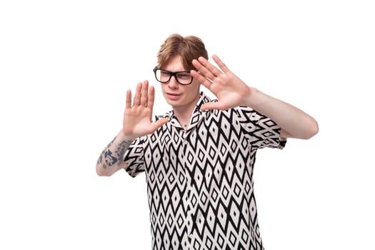 young caucasian ginger man with a tattoo on his arms dressed in a black and white shirt shows a gesture of disagreement.