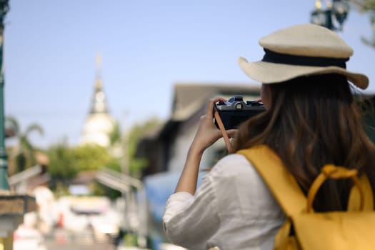 A young beautiful tourist with backpack taking photos with her camera of local city street in Chiang Mai, Thailand.
