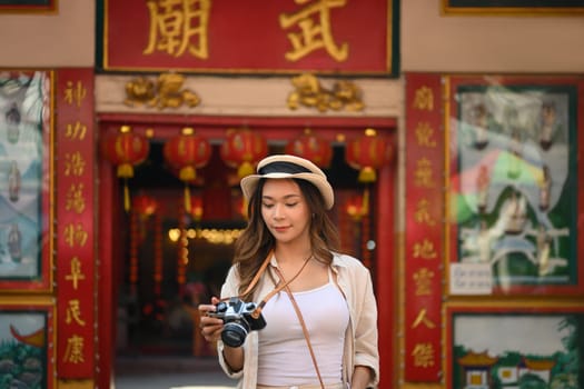 Beautiful female traveller with camera standing against a Chinese Temple located in Chang Mai Thailand.