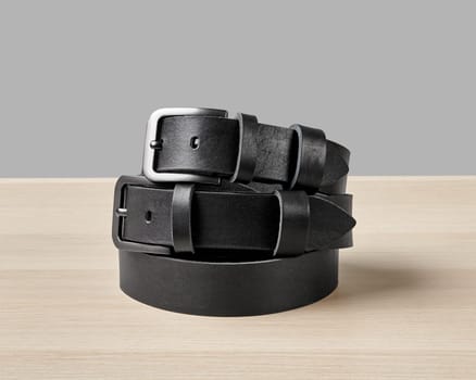 Two folded black leather belts featuring bespoke DAD embossing on loop merging personal style with artisan quality, stacked on wooden surface