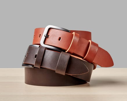 Closeup of folded terracotta and brown leather belts with custom DAD embossing on loop on wooden surface. Stylish mens accessories and personalized gifts