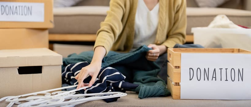 Donation, asian young woman sitting pack object at home, putting on stuff into donate box with second hand clothes, charity helping and needy people. Reuse recycle.