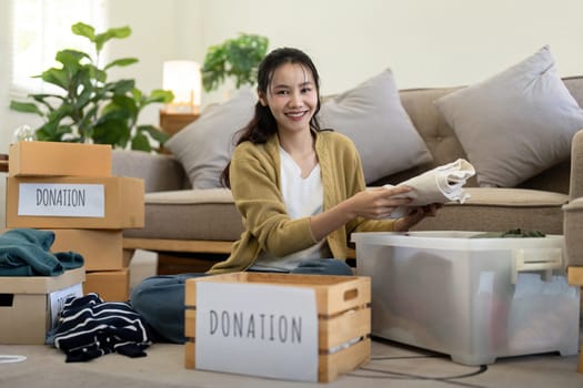 Woman asian holding donation box full with clothes and select clothes. Concept of donation and clothes recycling. Helping poor people.