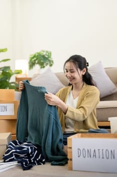 Woman asian holding donation box full with clothes and select clothes. Concept of donation and clothes recycling. Helping poor people.