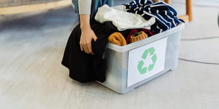 Asian women sort clothes from old clothing box to recycle. Recycling clothes concept.