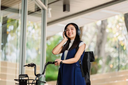 Asian young businesswoman bike to work for eco friendly green energy and listen music with headphone while commuting in city. Eco friendly.