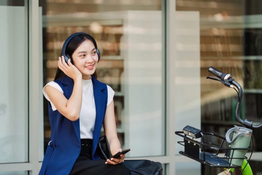 Smiling asian businesswoman hold reusable eco-friendly ecological cup and using mobile while sitting at park.