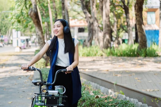 Asian young businesswoman bike to work for eco friendly green energy and listen music with headphone while commuting in city. Eco friendly.