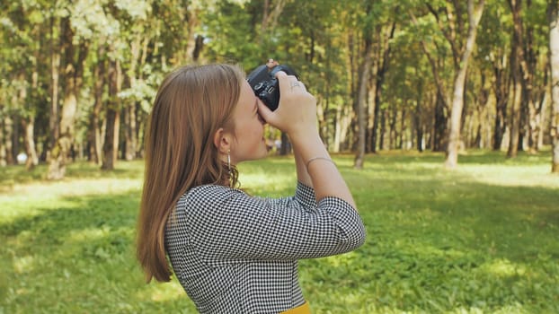 A young girl photographer with a camera poses in the park