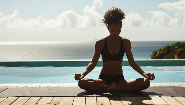 Young woman practicing yoga by a swimming pool with ocean in the background