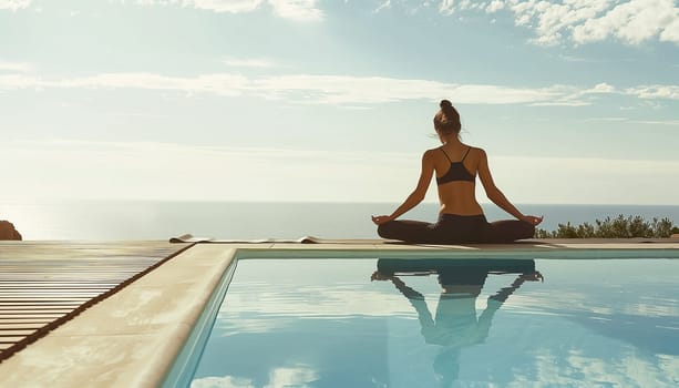 Young woman practicing yoga by a swimming pool with ocean in the background